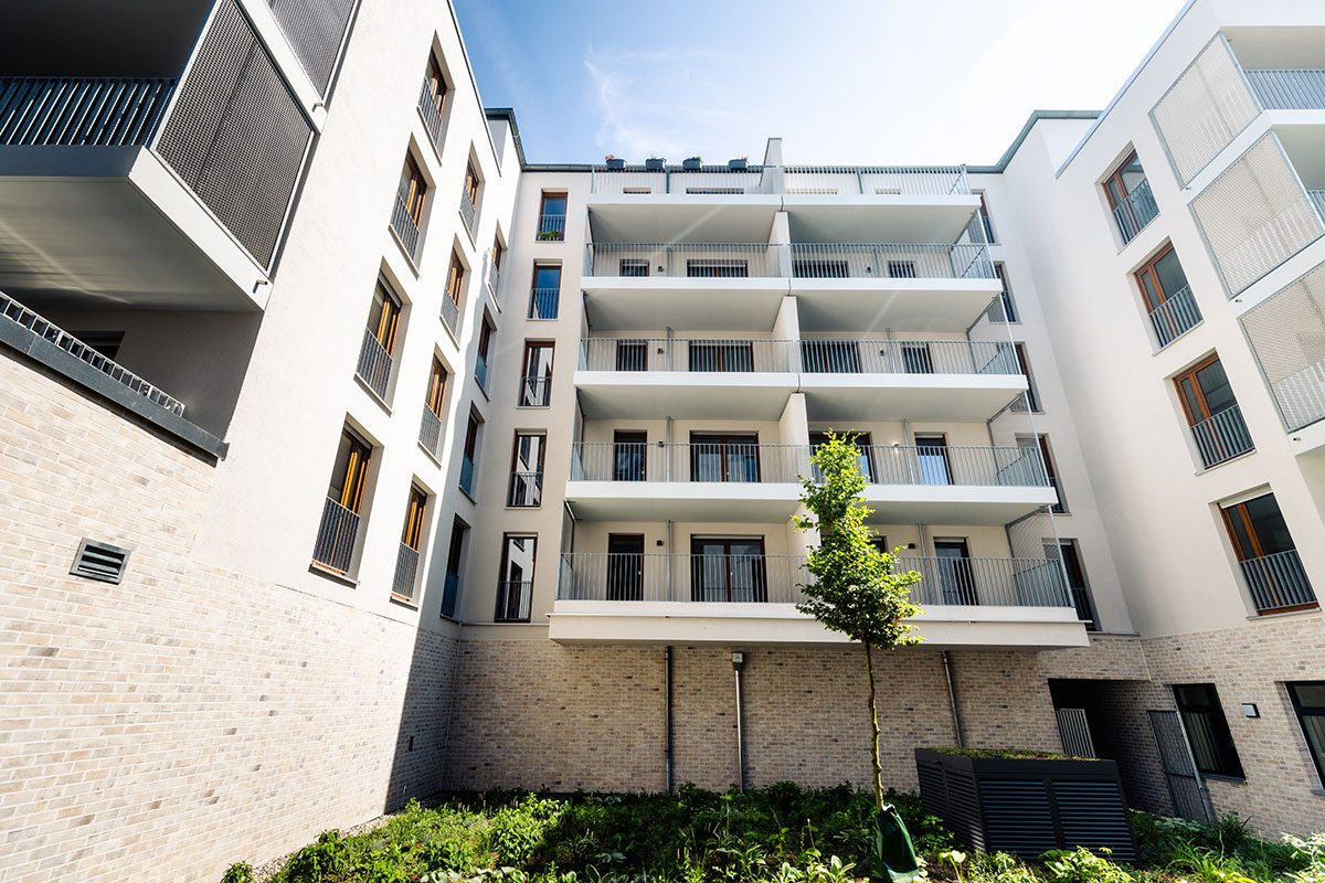 Hofseite mit übereinanderliegenden Balkonen und jungem Baum im Innenhof
